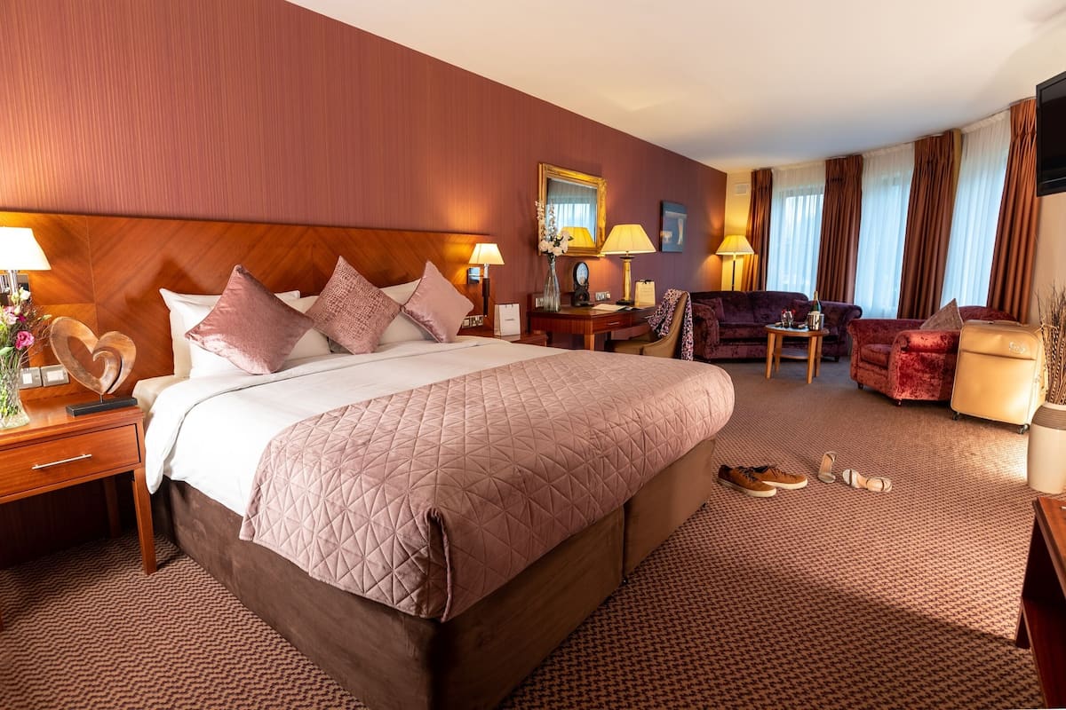 A hotel room with a large bed, a desk, a chair, a sofa, and a TV.