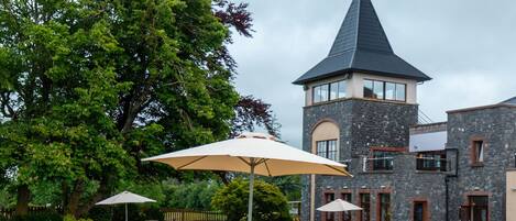 A courtyard with picnic tables and umbrellas, a stone building with a tower, and a large tree.