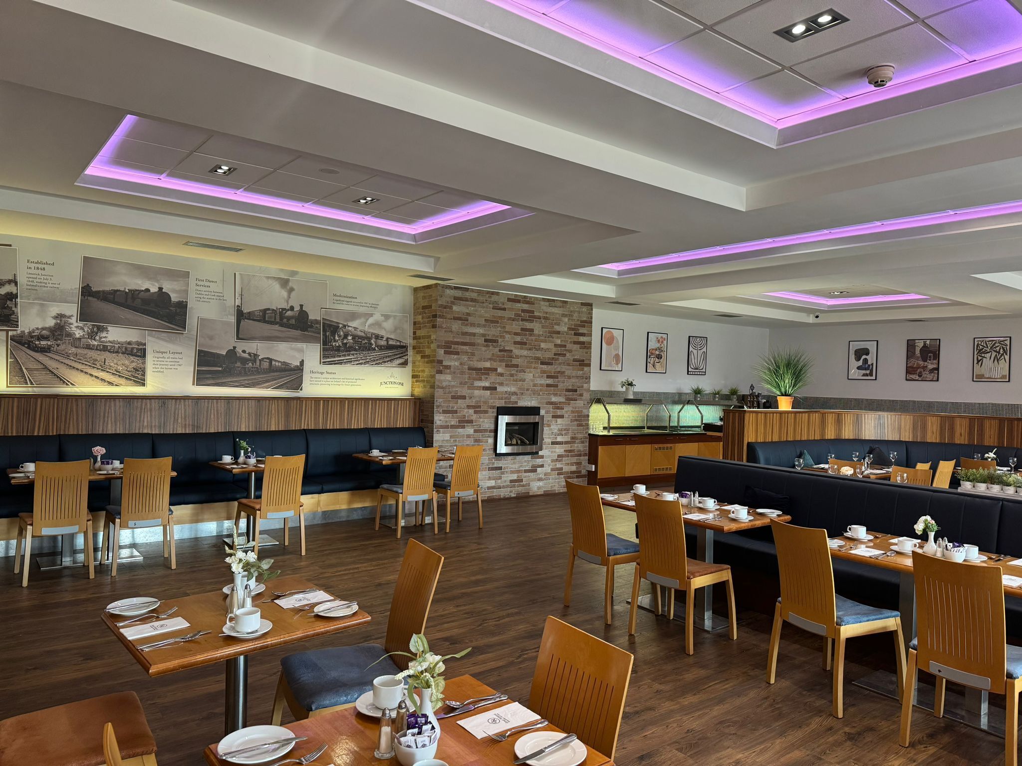 A restaurant with wooden tables and chairs, a brick wall, and a neon ceiling.
