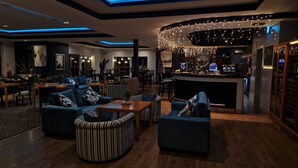 Un área de lounge moderna con sofás, una mesa de centro y una zona de bar con luces colgantes.