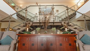 Un área de recepción con un mostrador de madera, barandales de vidrio y una escalera.