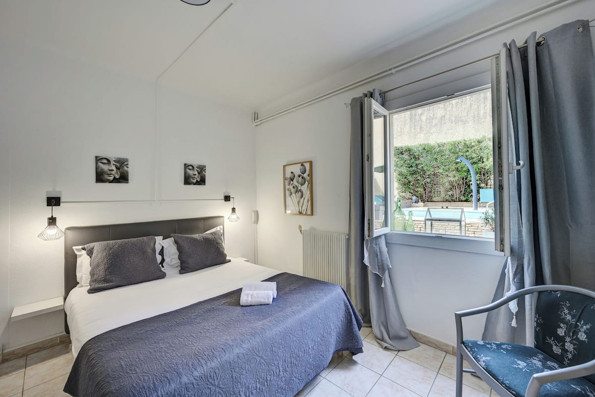 Quarto com cama, uma cadeira e vista para uma piscina.