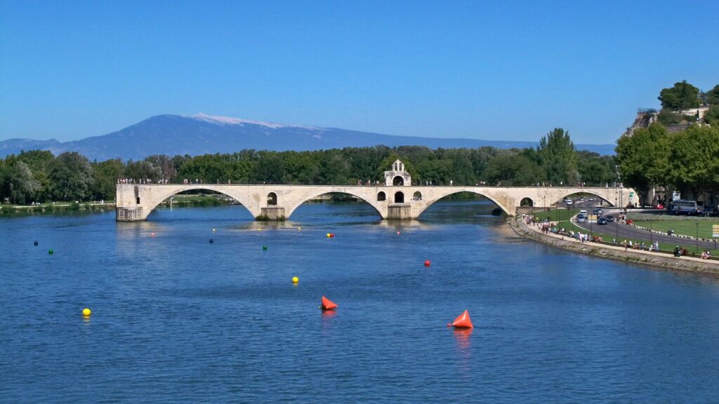 A stone bridge over a calm river with a mountain in the background.
