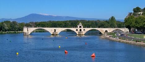 A stone bridge over a calm river with a mountain in the background.