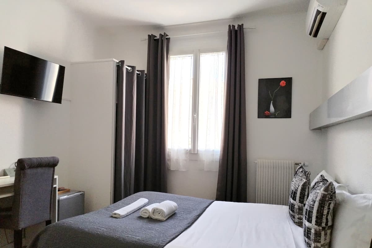 Quarto de hotel com cama, secretária, cadeira, televisão e radiador.