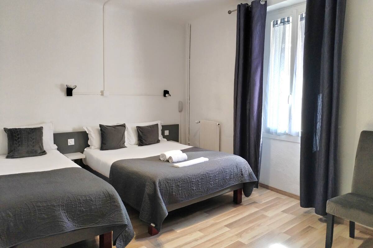 Quarto de hotel com duas camas, piso de madeira, janela com cortinas, radiador e telefone na parede.