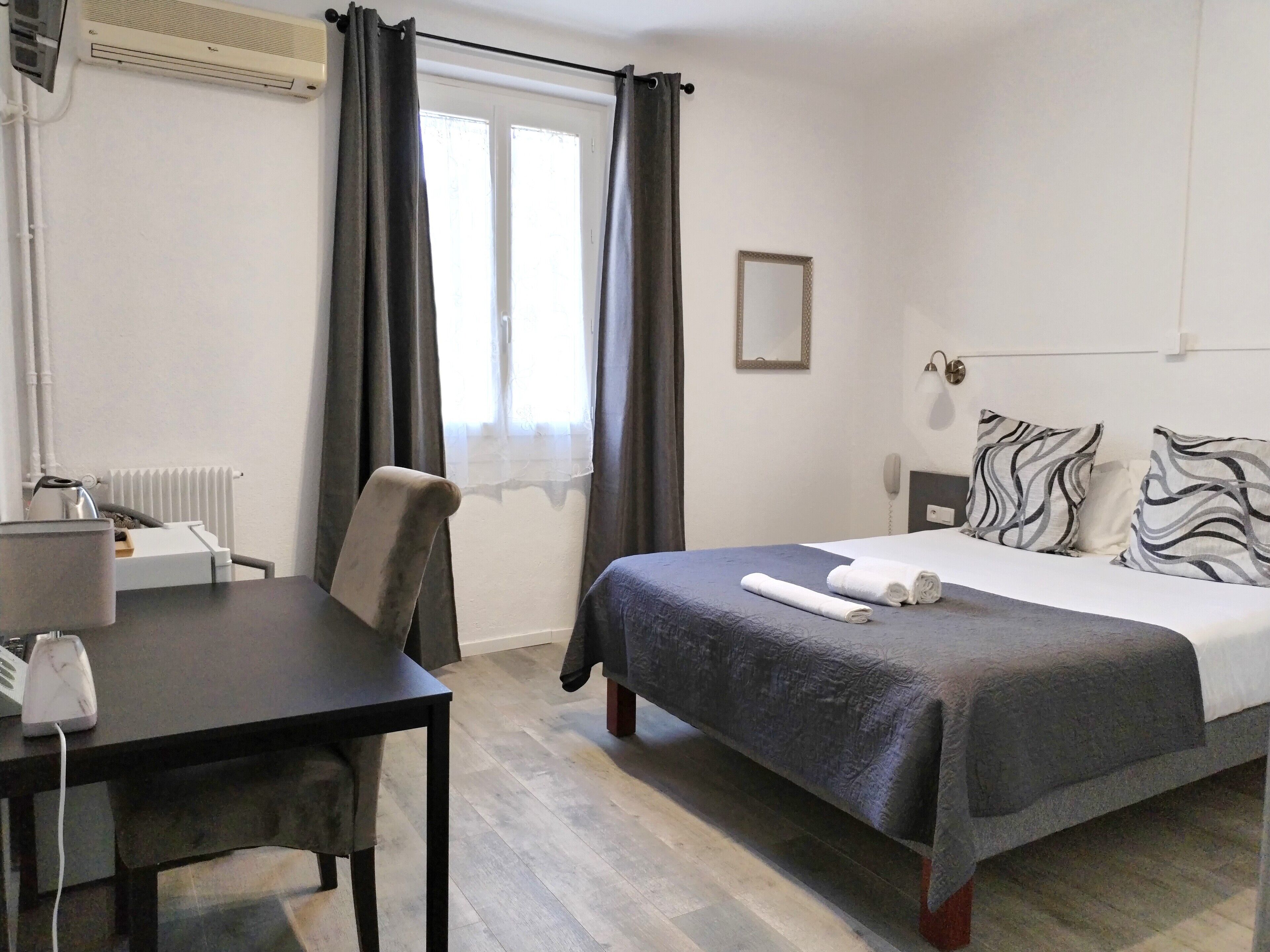 Une chambre d’hôtel équipée d’un lit, d’un bureau, d’une chaise, d’un radiateur, d’un téléphone et d’une fenêtre avec des rideaux.
