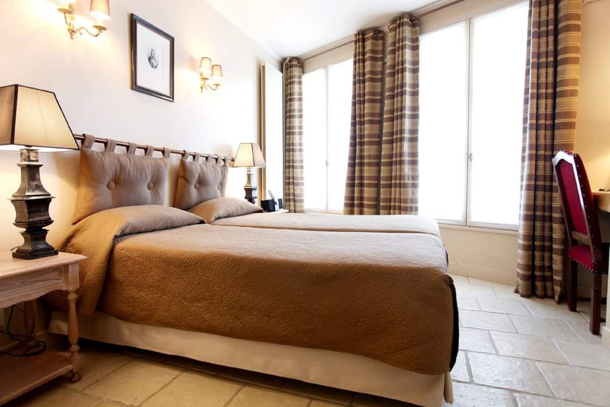 A double bed with a headboard, bedside lamps, a framed picture on the wall, and a window with curtains.