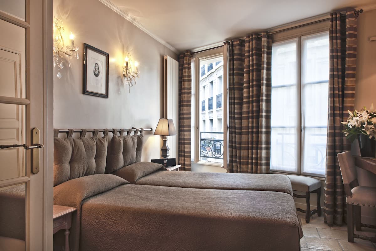 A hotel room with two beds, a chandelier, a framed picture on the wall, and a window with curtains.