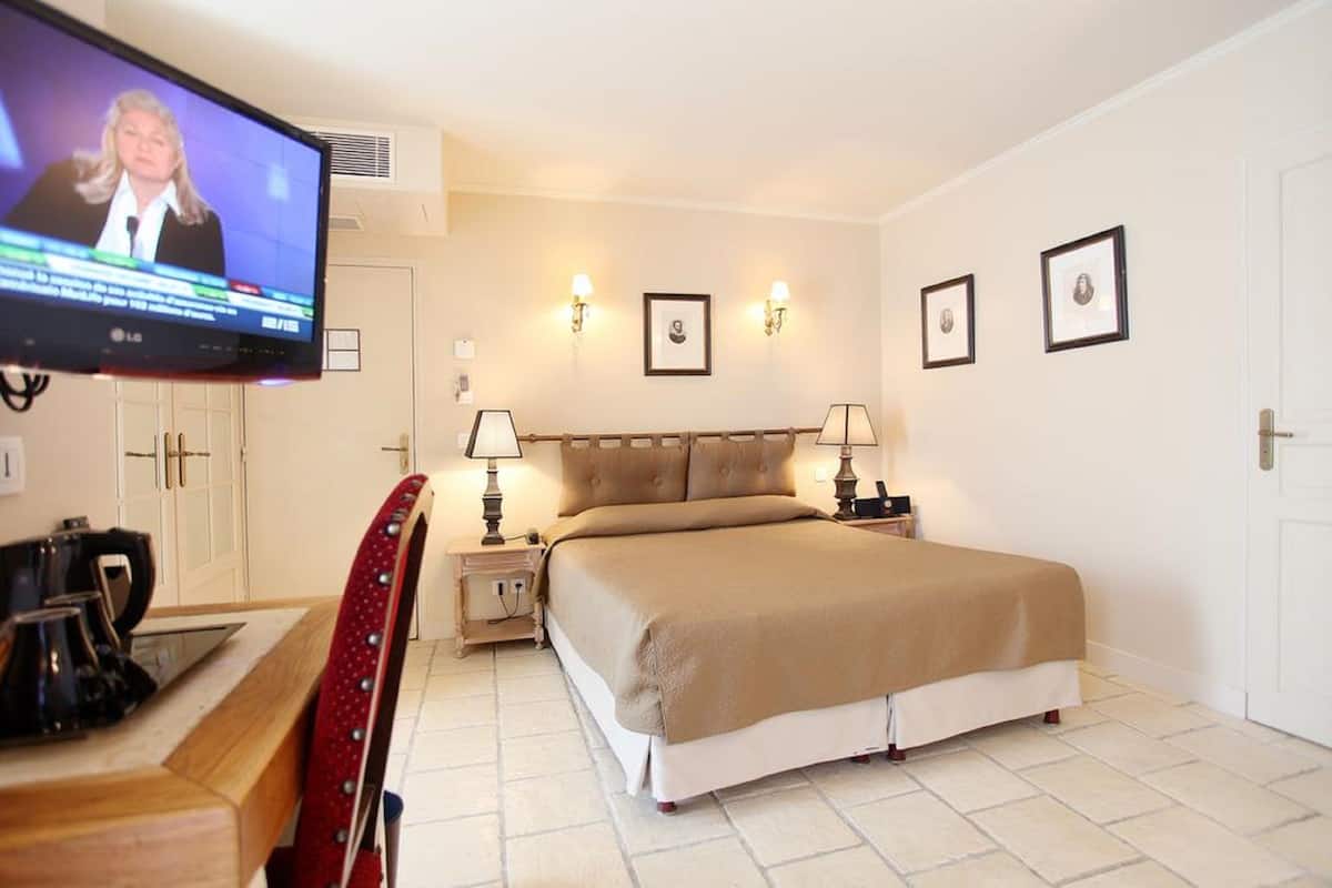 A hotel room with a bed, bedside tables, a TV, and wall-mounted lights.