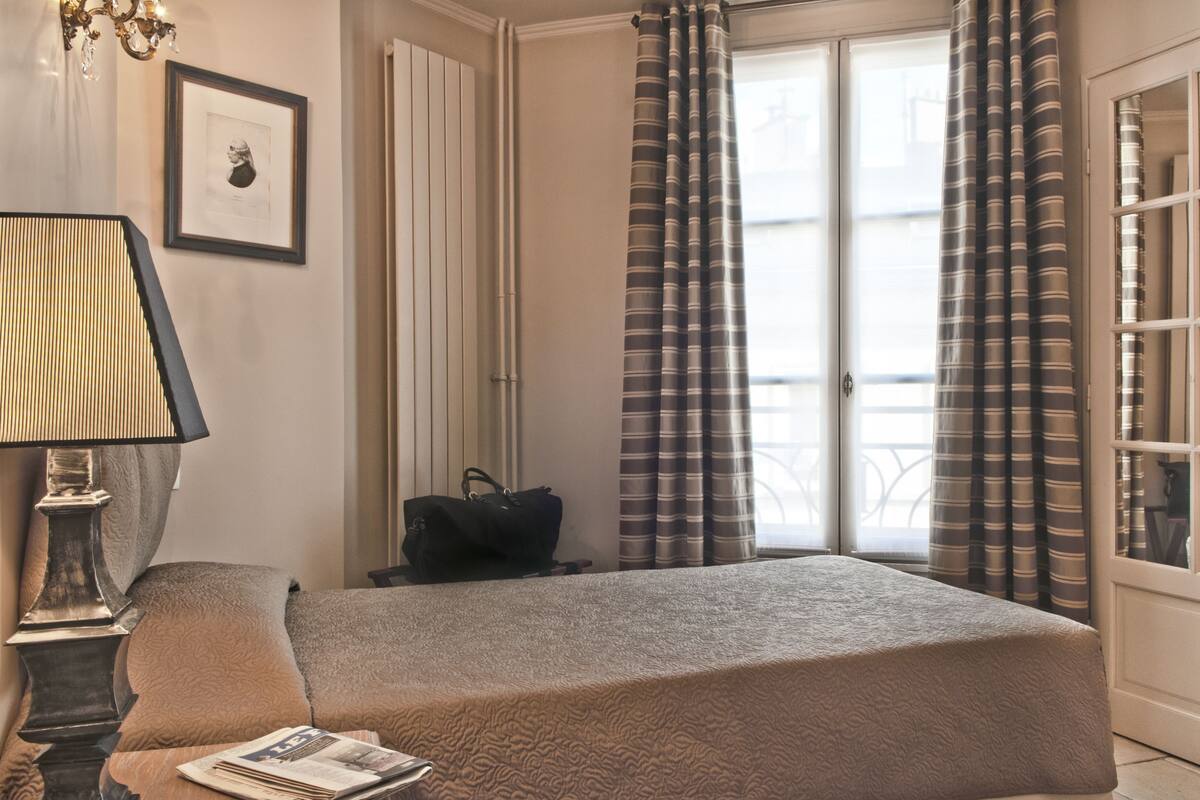 A hotel room with a bed, a lamp, a framed picture on the wall, and curtains.
