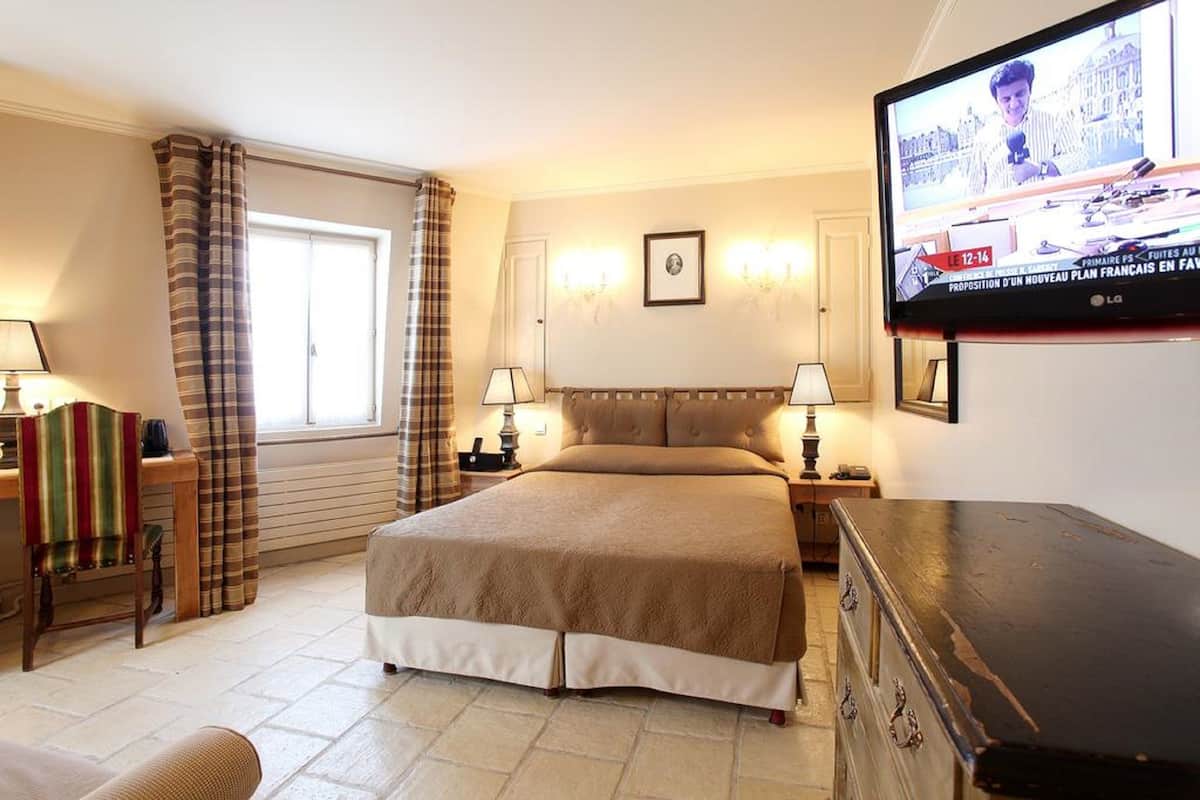 A hotel room with a large bed, a television mounted on the wall, and a window with curtains.