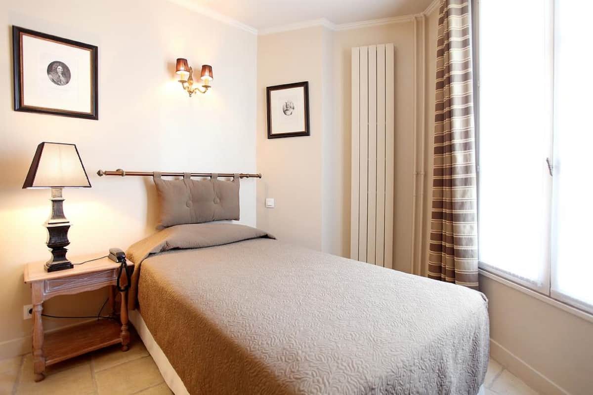 A neatly arranged bedroom with a bed, bedside lamp, framed pictures, and a window with curtains.
