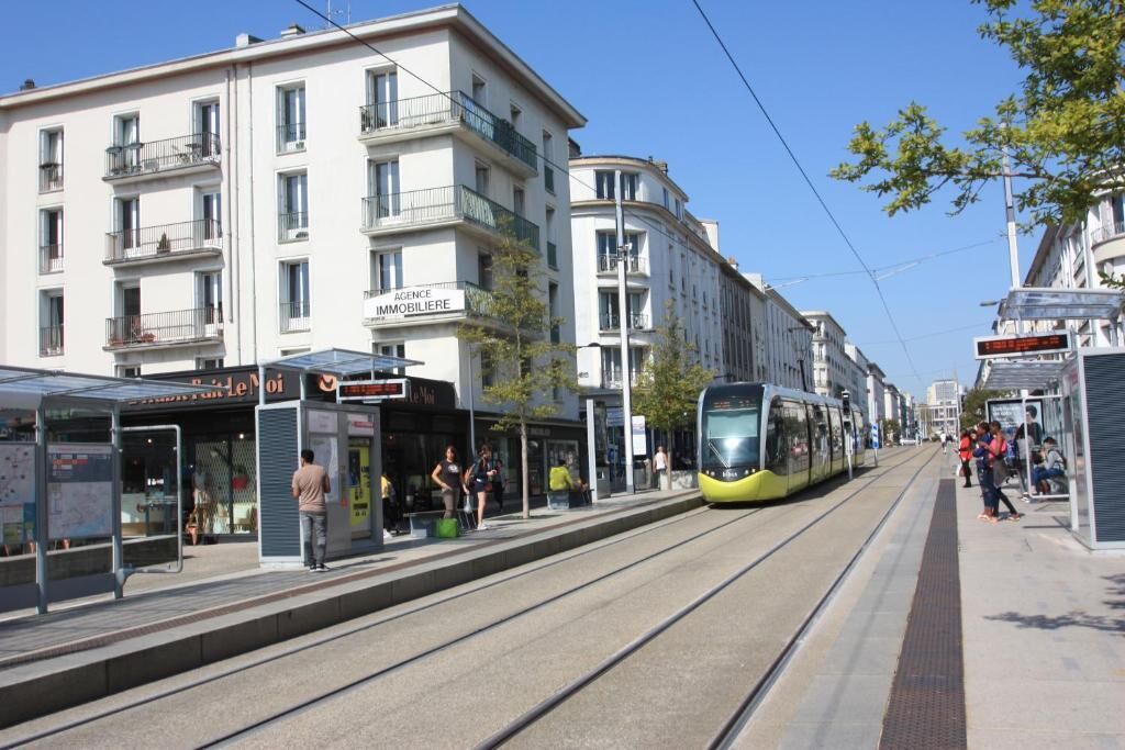 Une station de tramway avec un bâtiment moderne doté de balcons et d’une enseigne indiquant « Immobilier ».