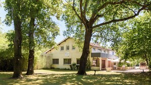 A two-story building with a sign indicating it is a hotel and restaurant. There are large trees in front of the building, and a patio area with outdoor furniture. - Hôtel Le Pont Bernet (Le Pian-Medoc)