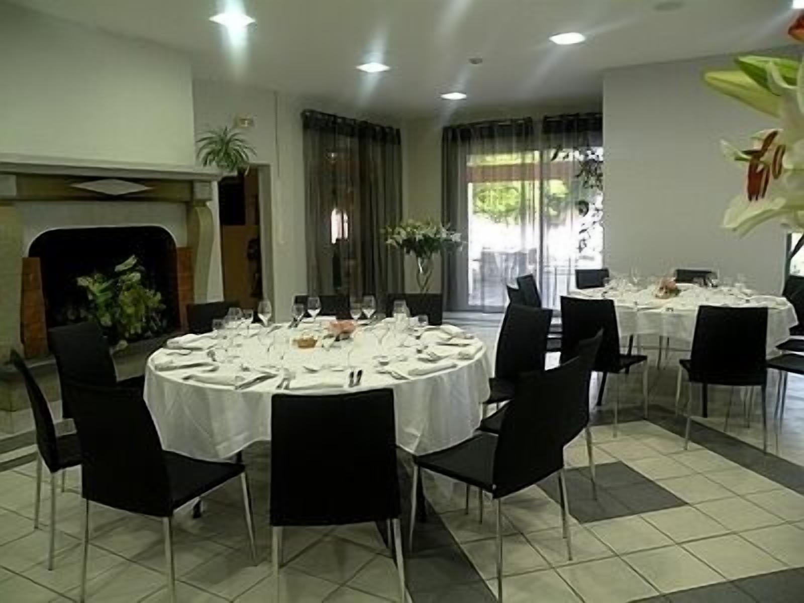 Un espace repas avec des tables rondes dressées pour le repas, des chaises noires et une cheminée en arrière-plan.