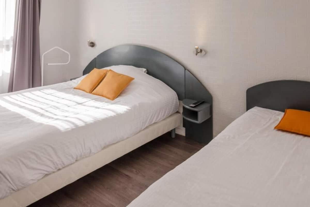 A hotel room with two beds, a nightstand, and a wall-mounted light fixture.