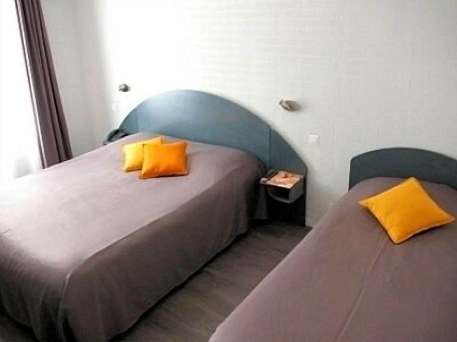 A hotel room with two beds, each with a pillow and a nightstand.