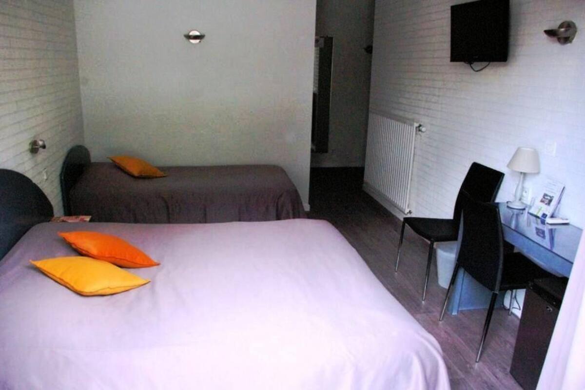 A small hotel room with a bed, two pillows, a desk with a chair, a TV, and a radiator.