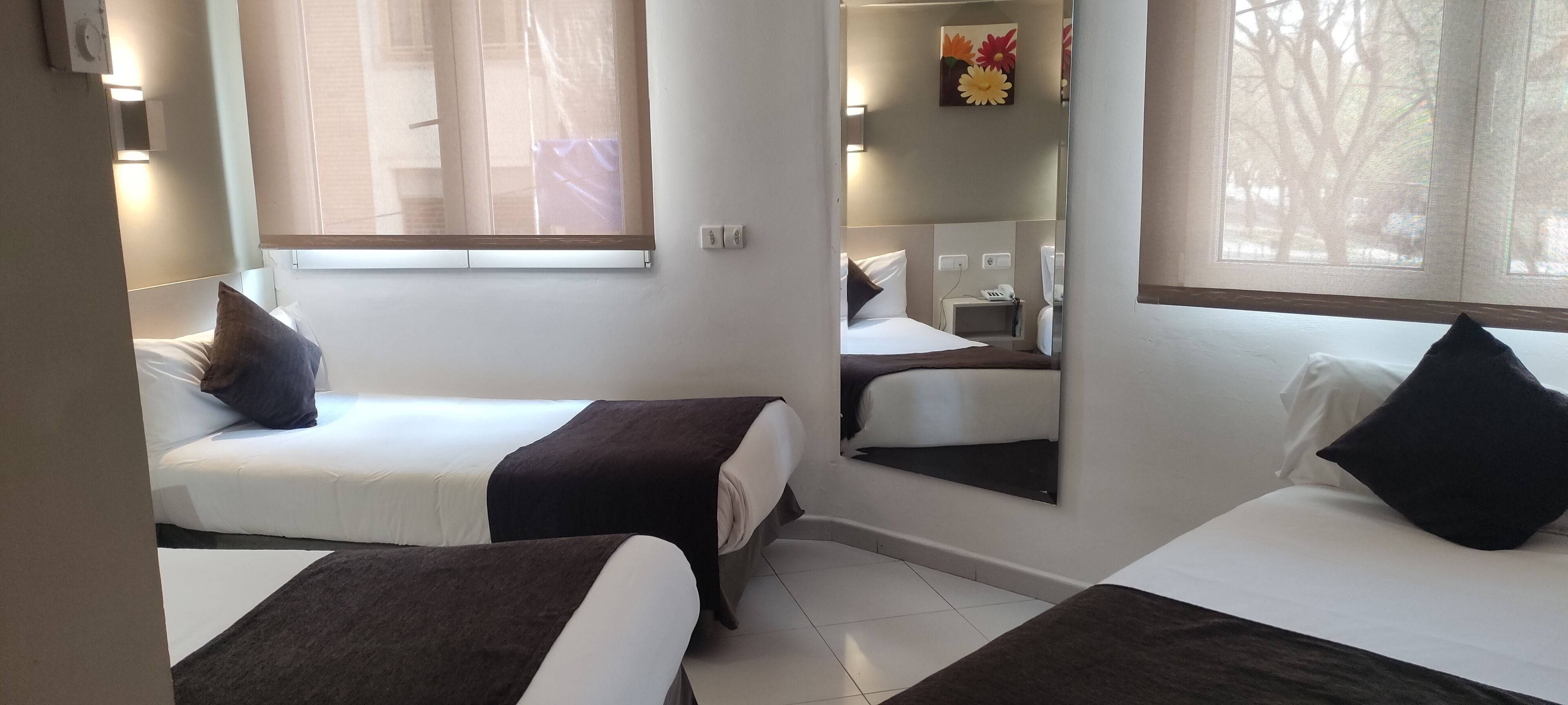 A hotel room with two beds, a large mirror, a telephone, and a window with blinds.