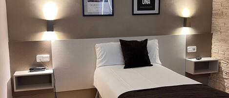 A modern hotel room with a bed, bedside tables, and two wall-mounted light fixtures.