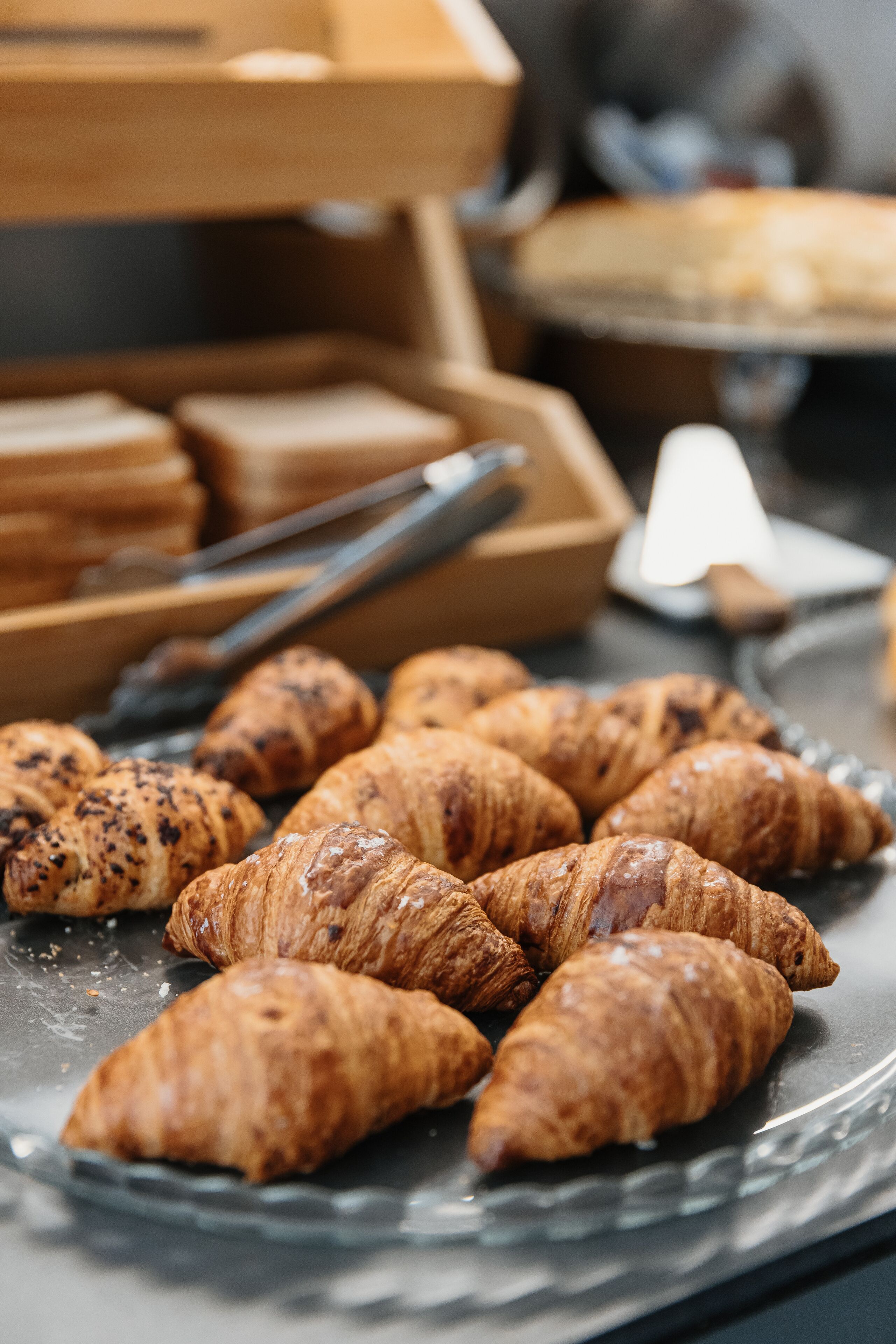 A glass plate with croissants and a wooden box with bread.