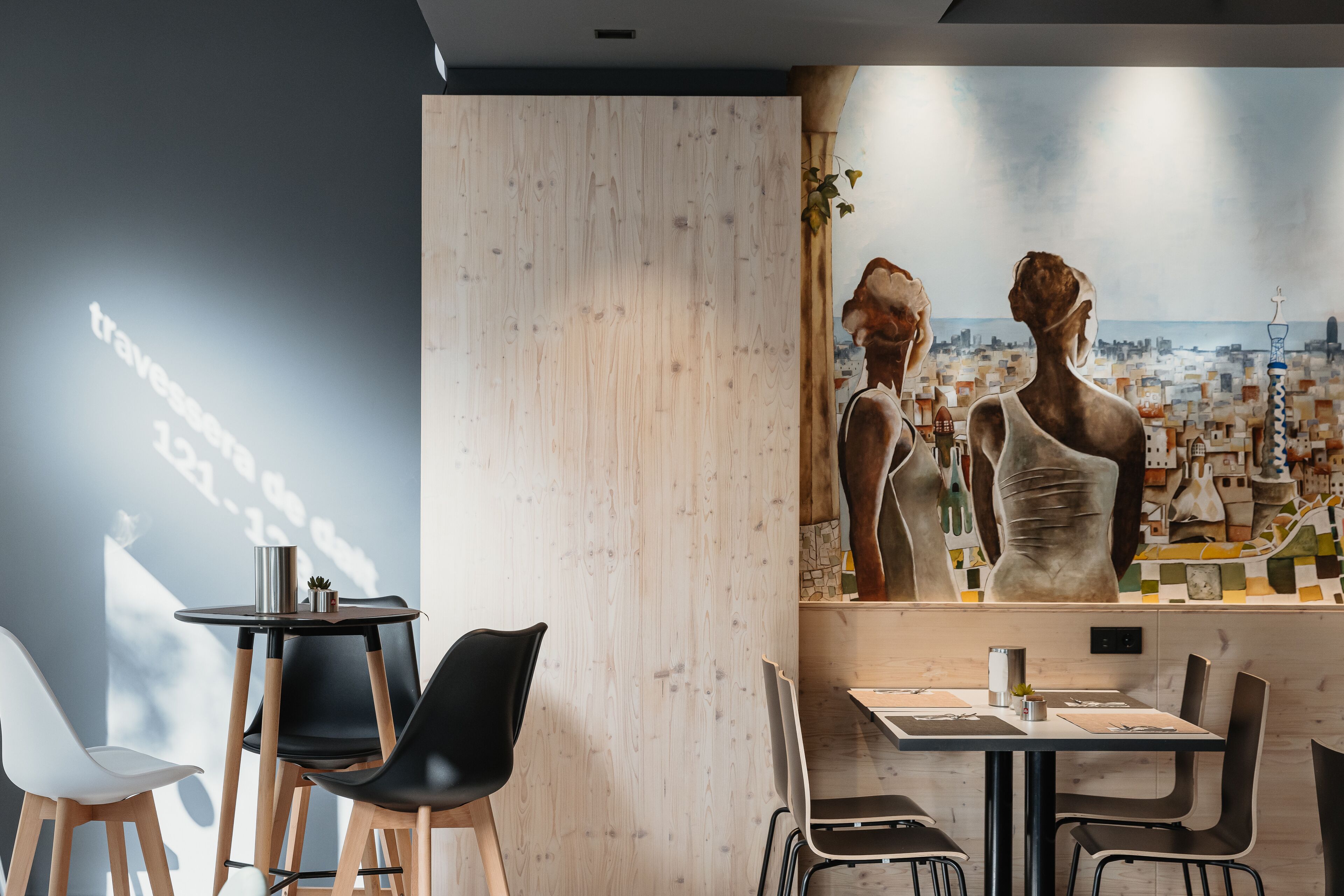 Un comedor moderno con separador de madera, sillas negras y blancas, y una mesa con un proyector mostrando texto.