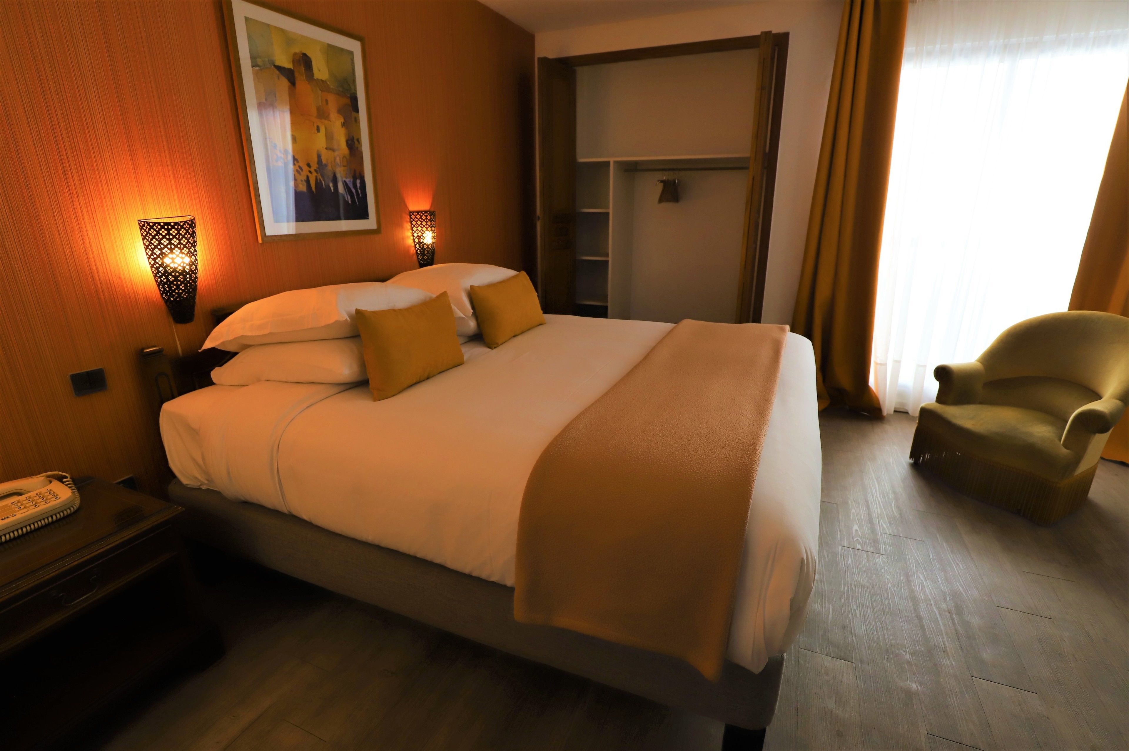 A hotel room with a bed, bedside table, lamp, and a chair.