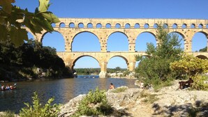 Un puente de piedra con múltiples arcos sobre un río, rodeado de vegetación y terreno rocoso.