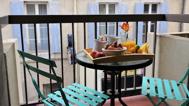 Un balcón con una mesa dispuesta para el desayuno, que incluye frutas, pan y una flor.