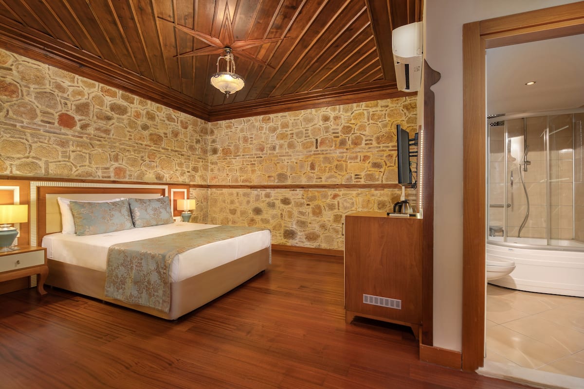 Ein Schlafzimmer mit Steinwand, Holzbalkendecke, einem Bett mit Kopfteil, Nachttischen und einem Beistelltisch.