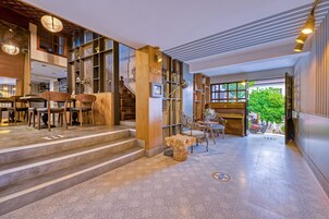 A spacious lobby with a staircase leading to upper floors, wooden furniture, and a view of greenery outside.