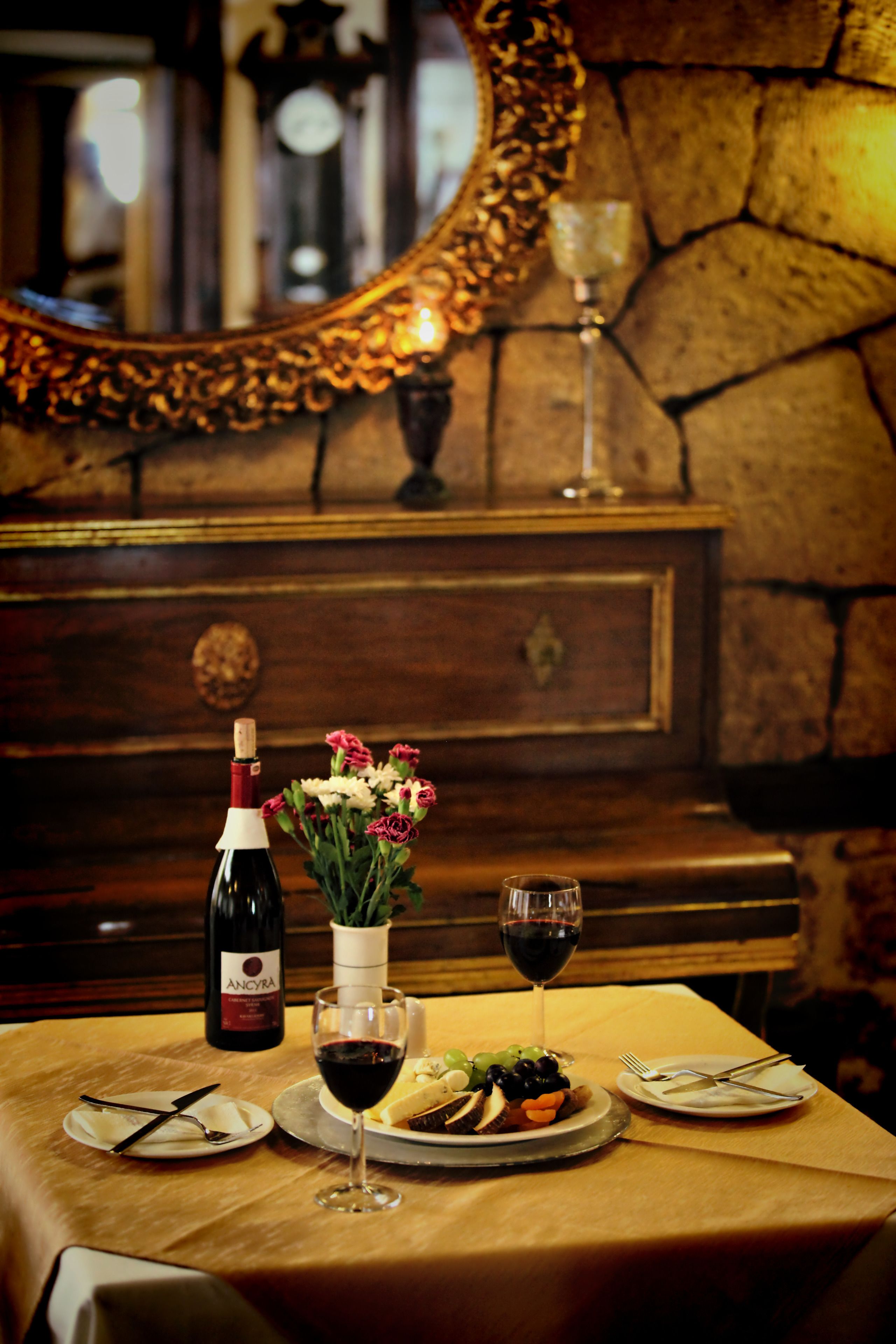 A table set with a bottle of wine, a glass of wine, a vase with flowers, and plates with food.