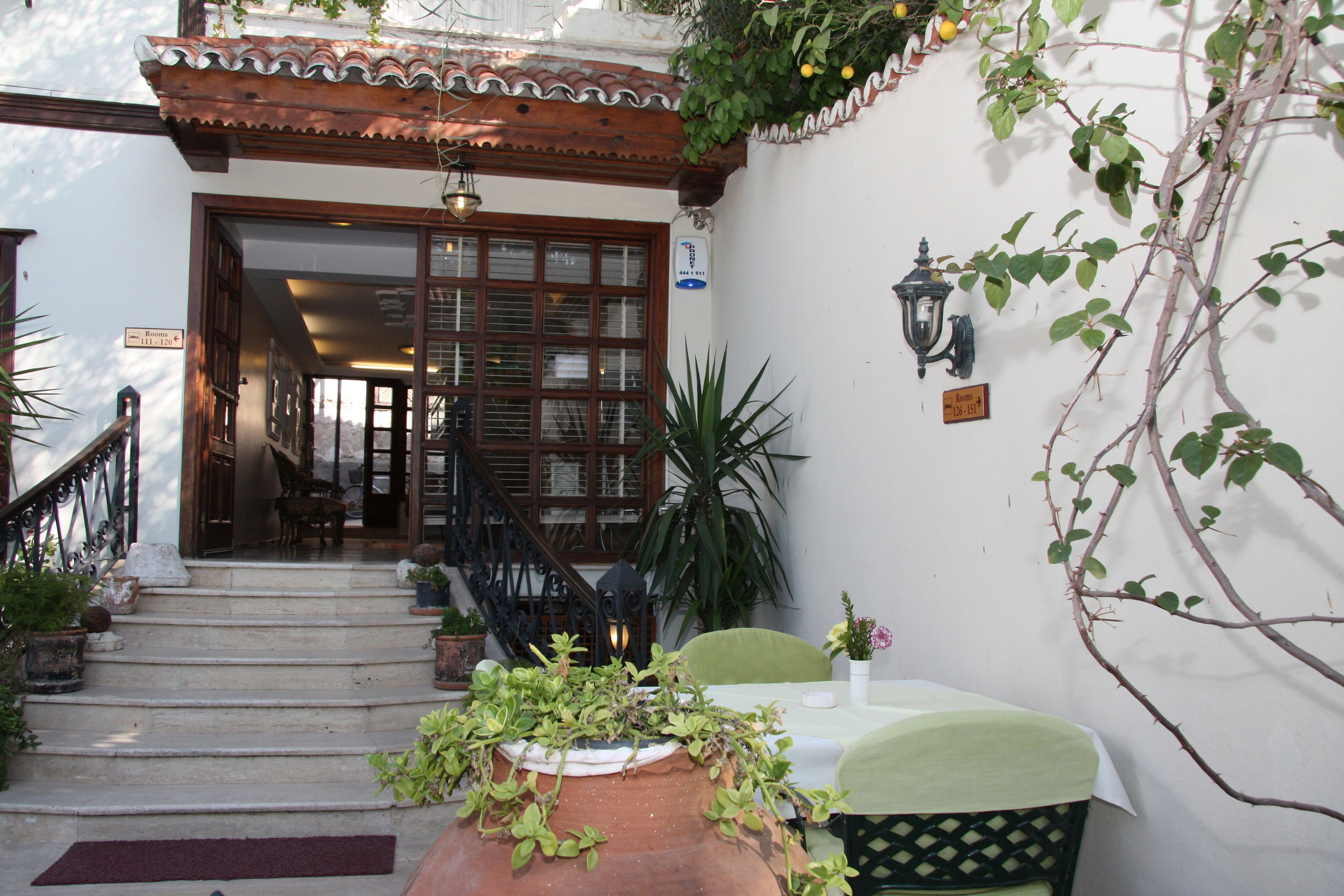 A hotel entrance with a tiled roof, a staircase leading to the rooms, and a table with chairs outside.