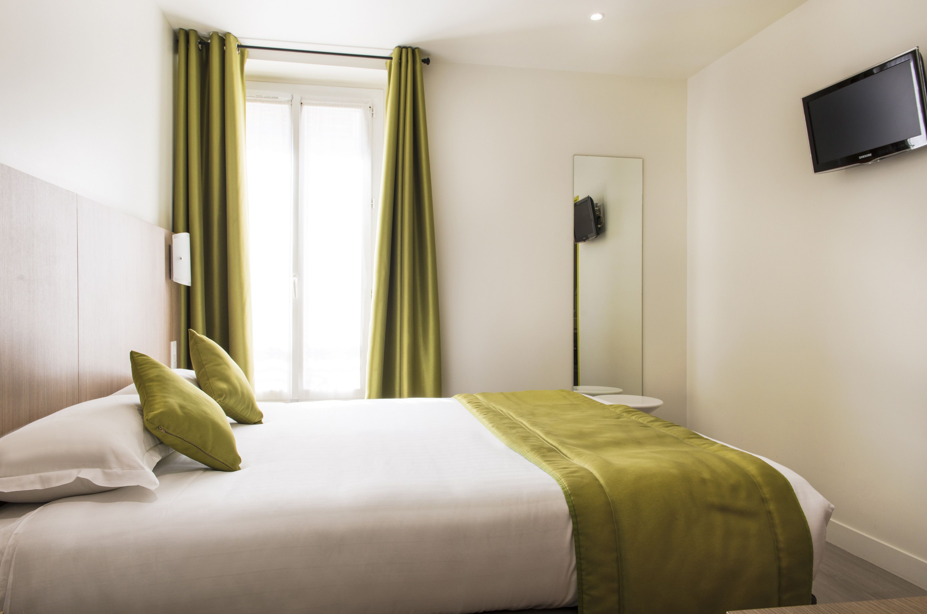 A hotel room with a bed, green curtains, a television, and a mirror.