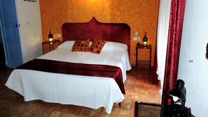 A hotel room with a large bed, two bedside tables with lamps, an orange textured wall, and a blue door. - Hotel La Fonda del Califa (Arcos de la Frontera)