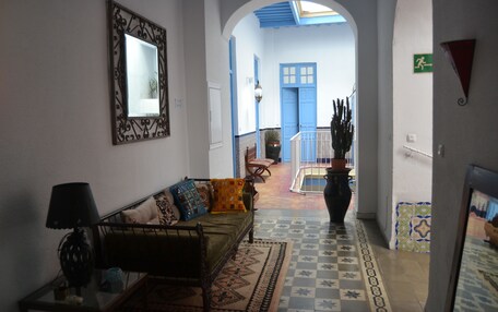 A hallway with a sofa, a lamp, and a mirror. There is a door leading to another room.