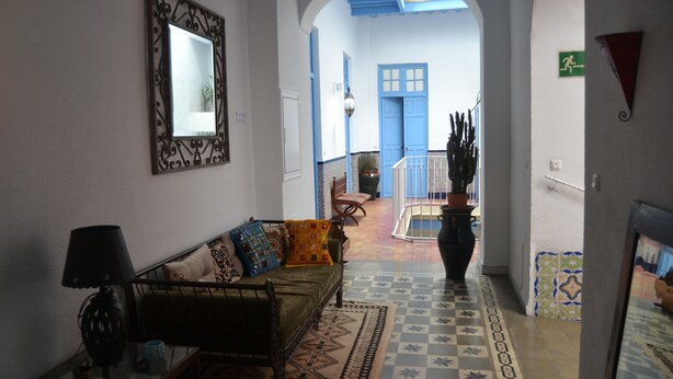 A hallway with a sofa, a lamp, and a mirror. There is a door leading to another room. - Hotel La Fonda del Califa (Arcos de la Frontera)