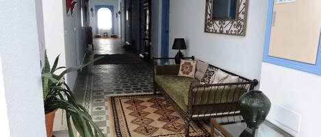 A hallway with a patterned floor, a sofa with cushions, a mirror, and a potted plant.