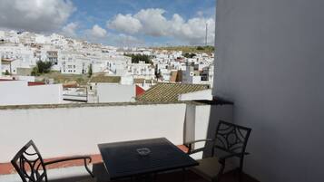 A balcony with a table and chairs, overlooking a densely packed town with white buildings and a clear sky.