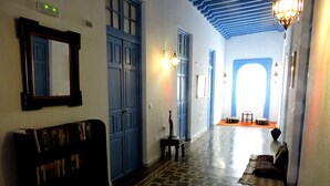 A hallway with patterned flooring, a bench with books, a door, and a view into another room. - Hotel La Fonda del Califa (Arcos de la Frontera)