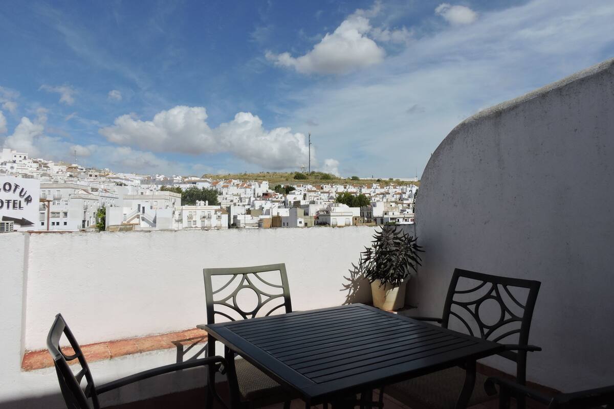 A terrace with a table and chairs, overlooking a town with white buildings and a clear sky.