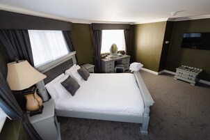 Habitación de hotel con una cama grande, un escritorio con espejo, una cómoda y un televisor en la pared.