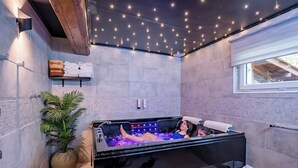 A modern bathroom with a large bathtub, a potted plant, and a ceiling with star-like lights. - Le Moulin de la Brevette (Arbigny)