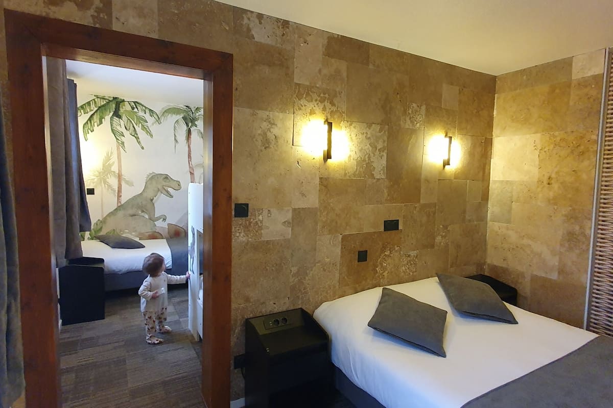 A bedroom with a bed, pillows, a nightstand, and a wall-mounted light fixture.
