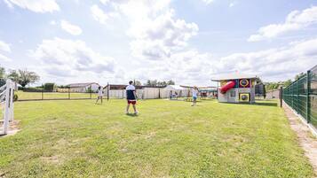 Un área recreativa al aire libre con una red de voleibol, una estructura de juegos y un perímetro cercado.