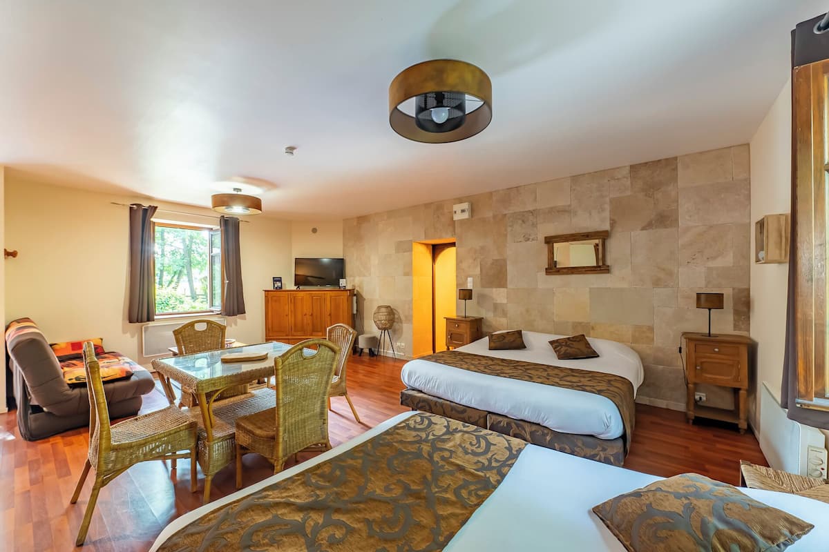 A hotel room with two beds, a dining area with wicker chairs, a television, and a stone wall.