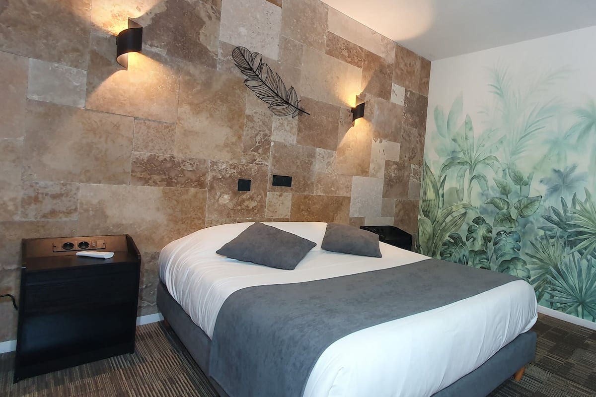 A modern bedroom with a large bed, a decorative wall, and a small desk with a cup.