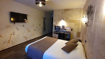 A hotel room with a bed, a flat-screen TV mounted on the wall, a desk with a chair, and a decorative wall piece.