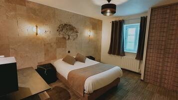 A hotel room with a bed, bedside table, lamp, and a wall-mounted tree decoration.